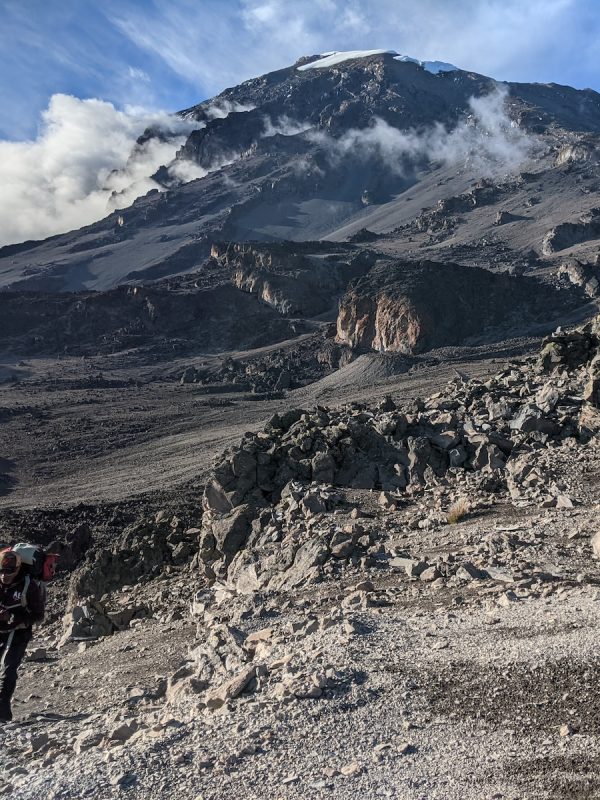 person in red jacket and black pants walking on rocky mountain during daytime